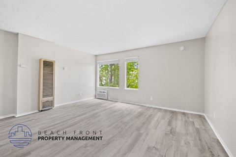 A spacious room with a wooden floor and a window overlooking greenery.