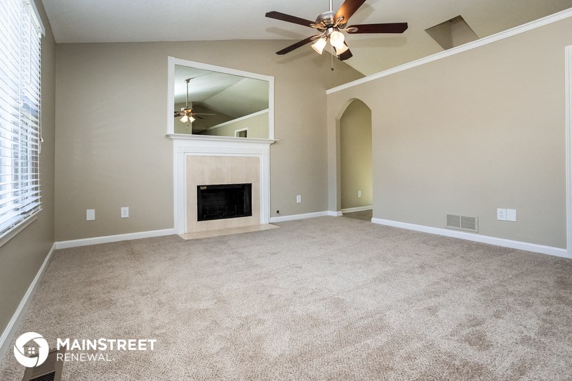 an empty living room with a fireplace and a ceiling fan