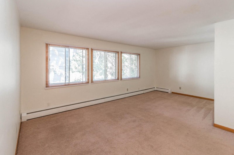 an empty living room with three windows and a carpet