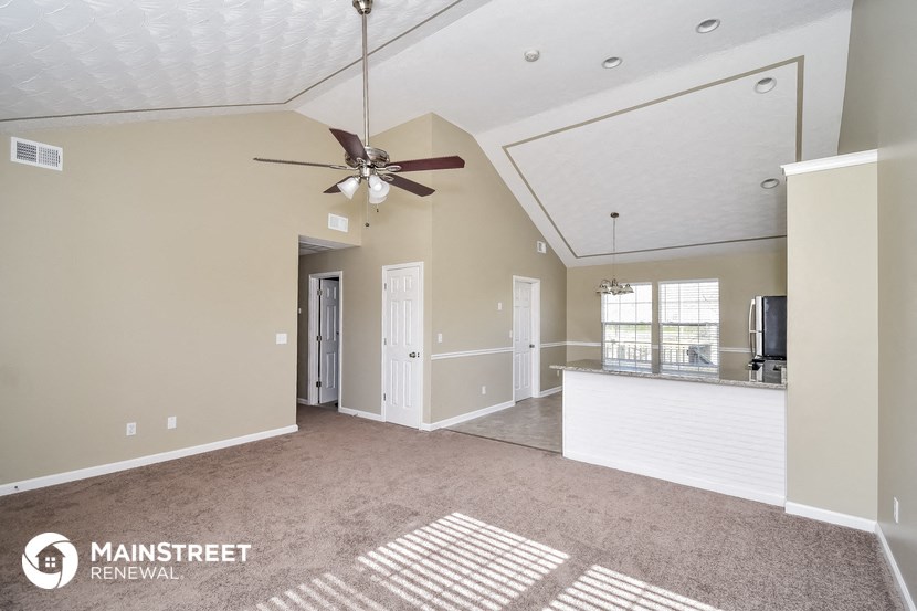 an empty living room with a ceiling fan and a kitchen