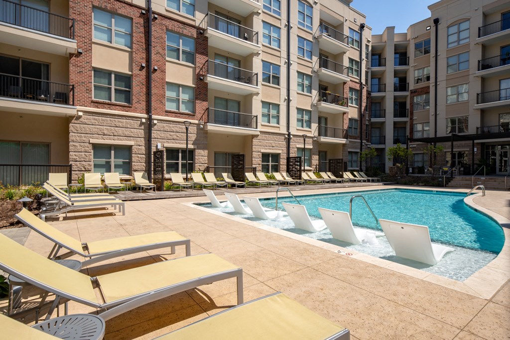 a swimming pool with lounge chairs in front of an apartment building