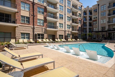 a swimming pool with lounge chairs in front of an apartment building