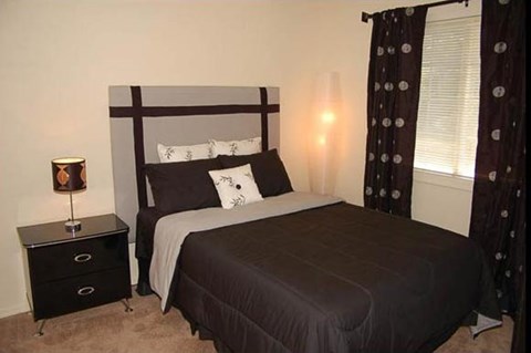 A bedroom with a bed, nightstand, and window.