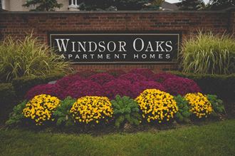a sign for windsor oaks apartment homes with flowers in front of it