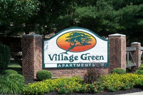 a sign for village green apartments in front of trees