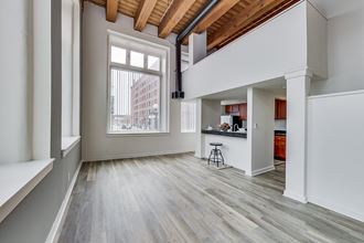 an empty living room with a large window and a kitchen in the background