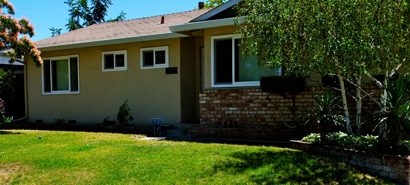 A house with a brown and beige exterior and a green lawn in front.