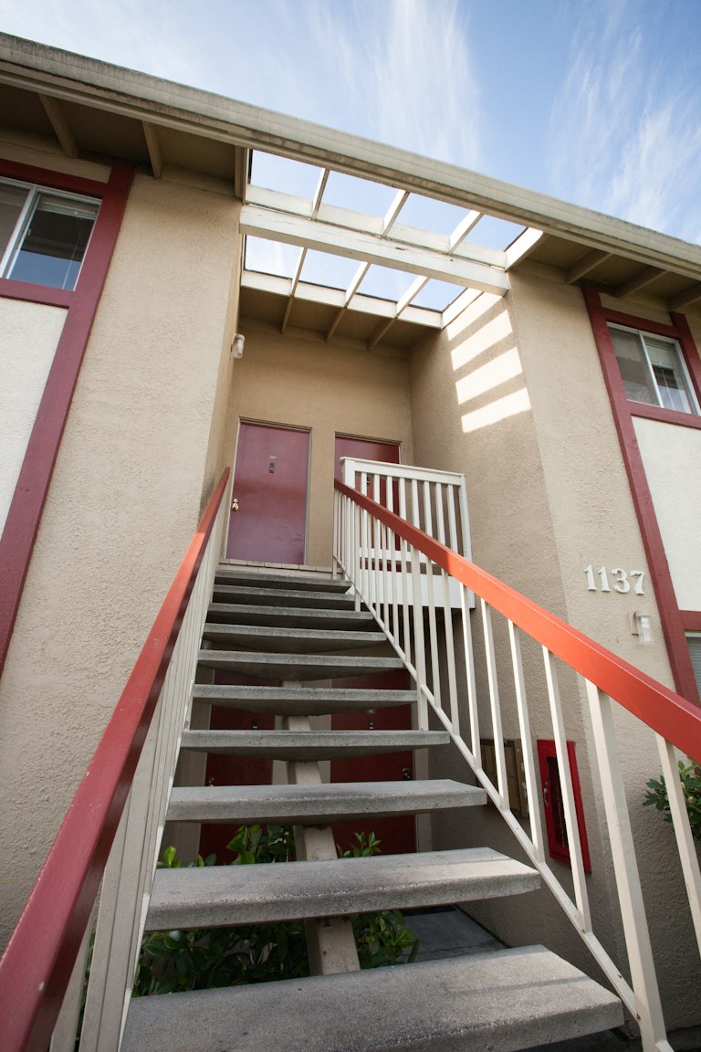 a red door on a tan building with red stairs and a white railing