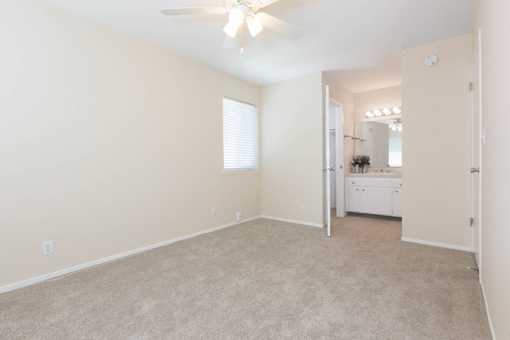 an empty bedroom with a ceiling fan and a bathroom in the background
