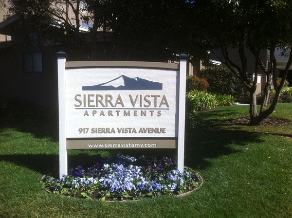 a sign apartments on the grass with flowers