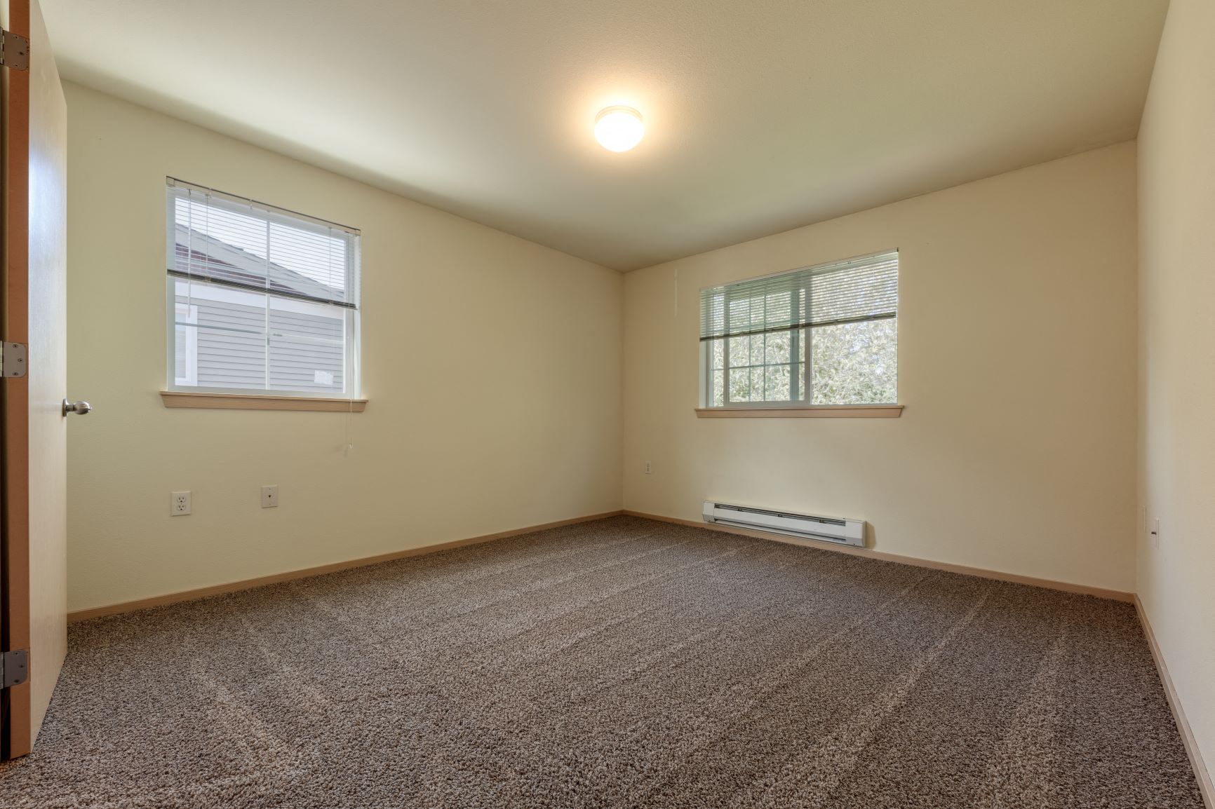an empty living room with two windows and carpet