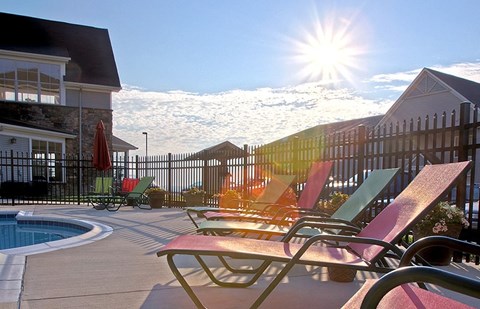 A sunny day at the pool with chairs and a fence.