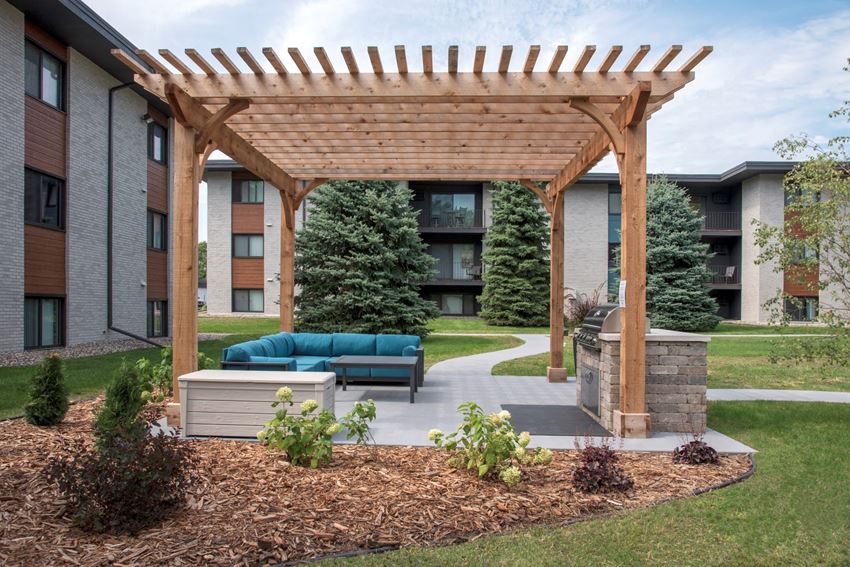 a wooden pergola with a couch and coffee table under it in front of an apartment