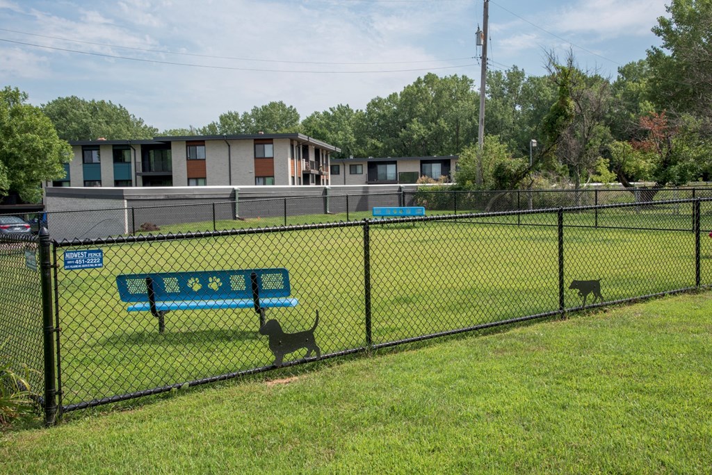 a park with a bench and two dogs behind a fence