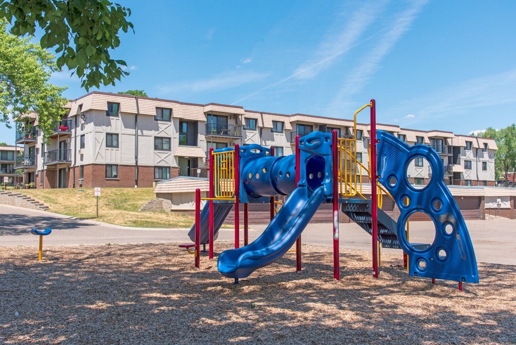 a playground with a blue slide in front of an apartment building