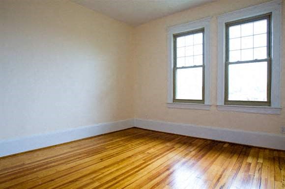 an empty room with wooden floors and two windows