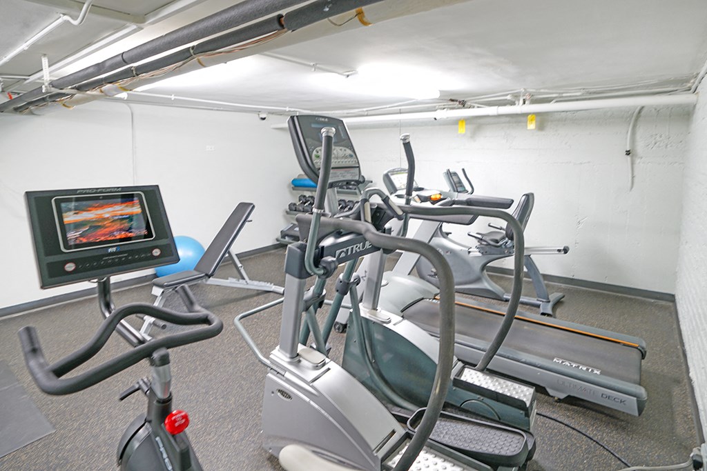 a gym with cardio equipment and a tv