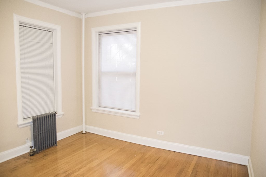a room with a wood floor and a radiator and two windows