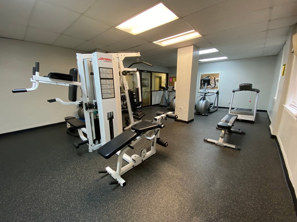 A gym with a variety of equipment including a squat rack, a leg press machine, and a bench press.