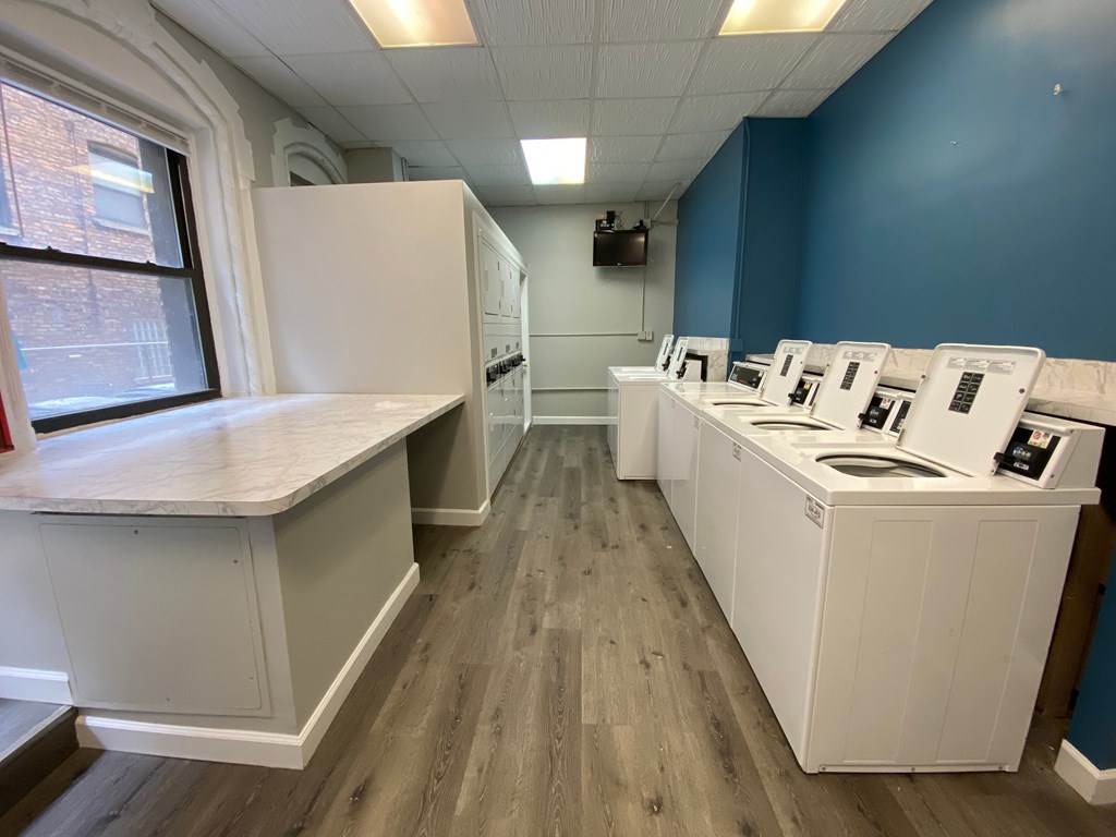 A row of white appliances are lined up in a room with wood floors and a window.