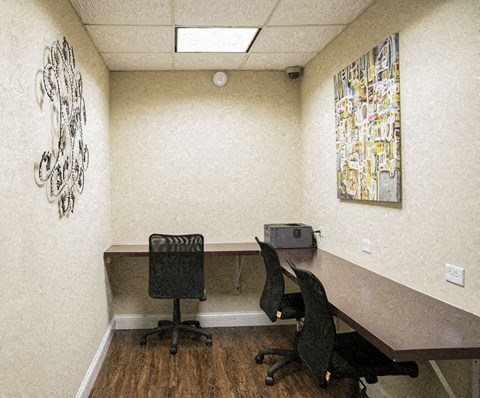 Two black chairs are in front of a desk with a large artwork on the wall.