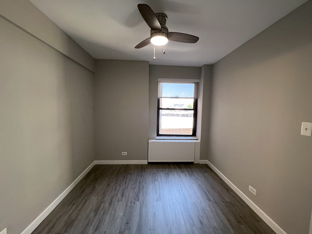 an empty living room with a window and a ceiling fan