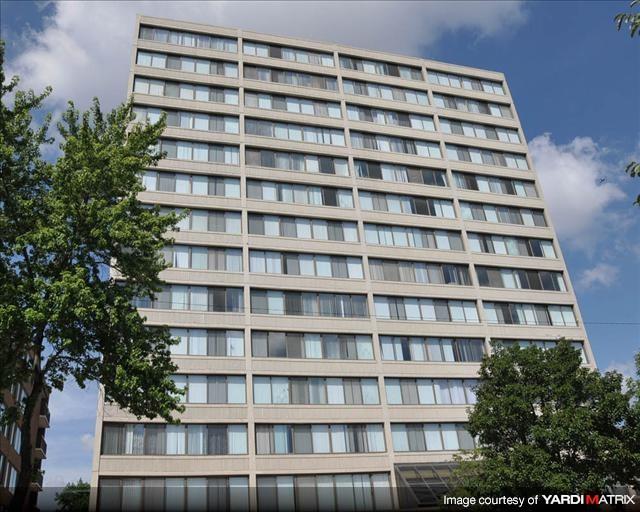 A tall building with many windows is surrounded by trees.