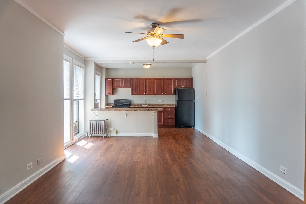 an empty living room with a ceiling fan and a kitchen