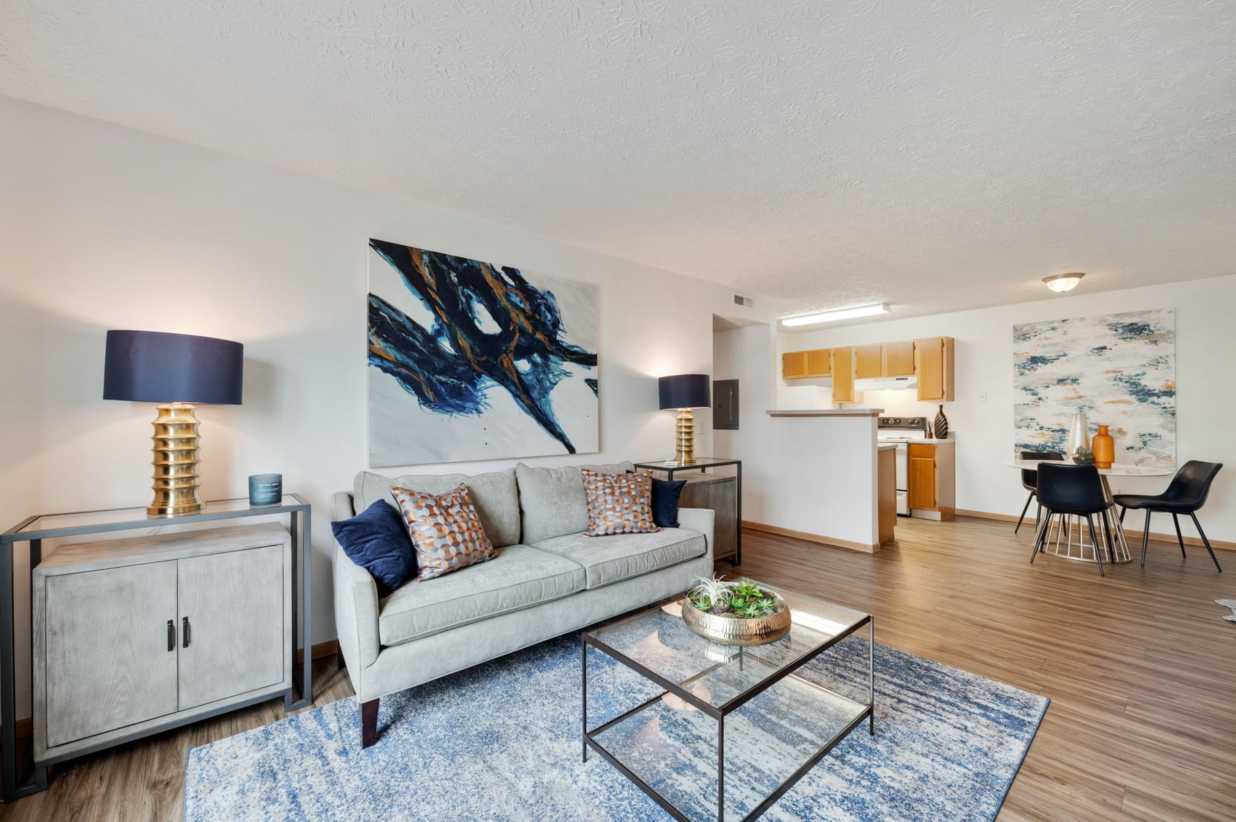 A modern living room with a grey couch, a glass coffee table, and a large abstract painting on the wall.