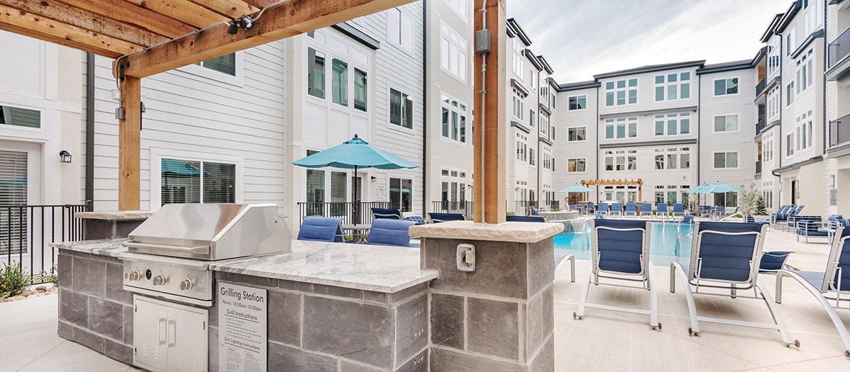 a patio with a grill and chairs and a pool