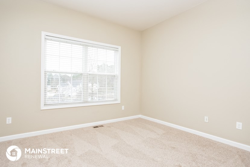 the upstairs bedroom has a large window and beige carpeting