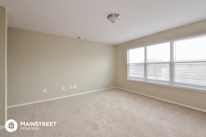 the spacious living room with two windows and beige carpeting
