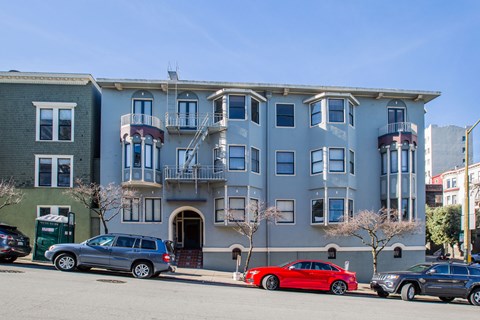 A grey building with a red car parked in front.