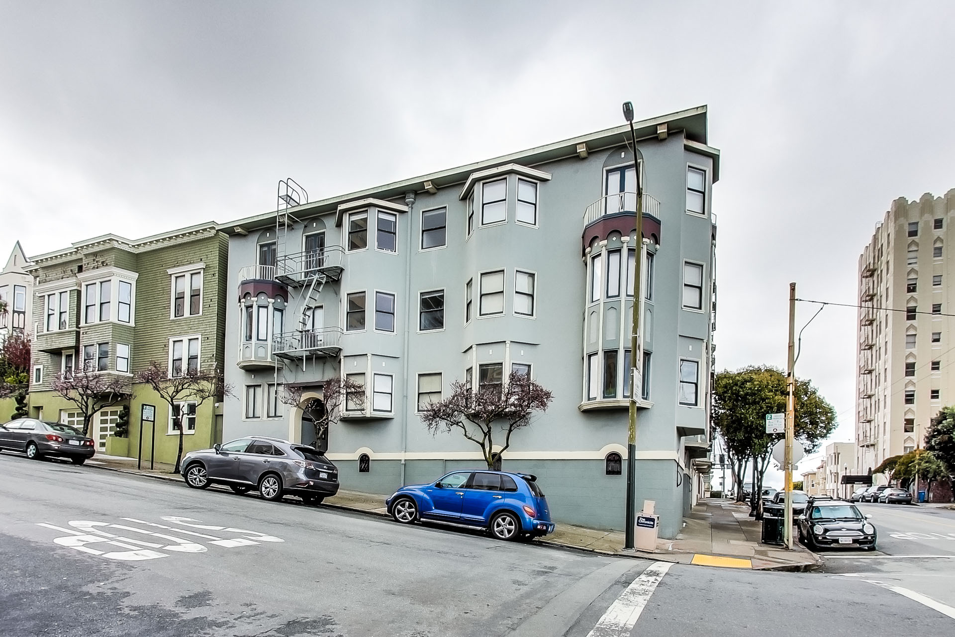 A street view of a row of three-story buildings with cars parked in front.