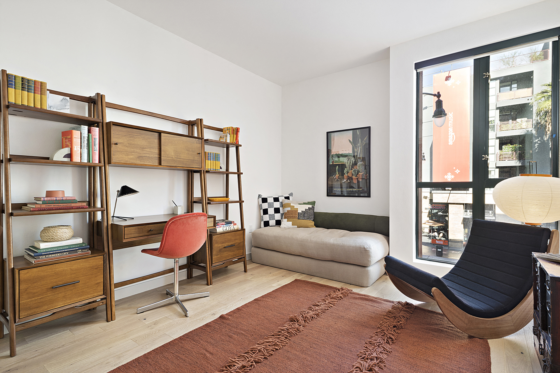 a living room with a bed and a desk with a chair and a book shelf