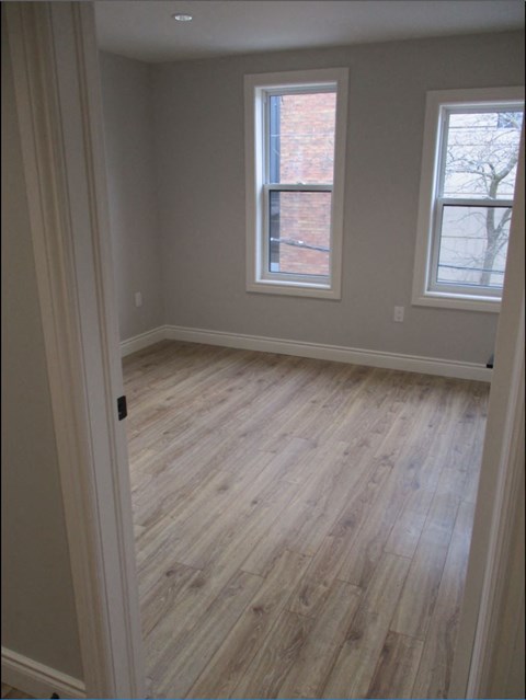 A room with light wood flooring and two windows.