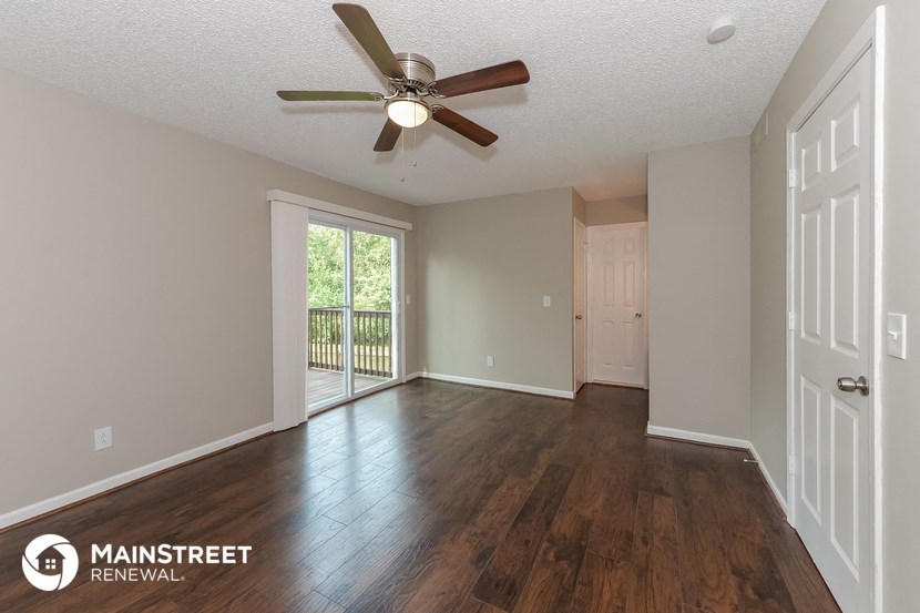the spacious living room with hardwood flooring and a ceiling fan