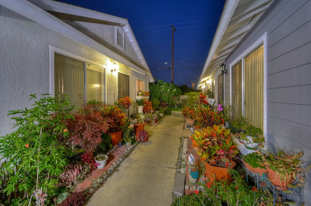a long sidewalk filled with potted plants next to a building
