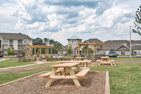 Picnic tables are set up in a grassy area in front of apartment buildings.