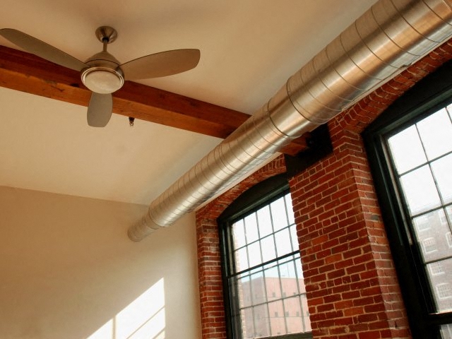 A room with a ceiling fan and a window with a brick wall.