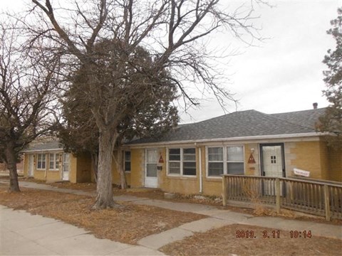 a yellow house with a porch and a tree in front of it