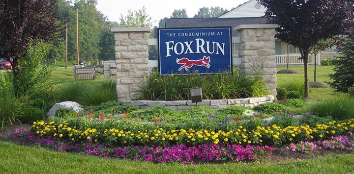 a sign for the fox run in front of a garden of flowers