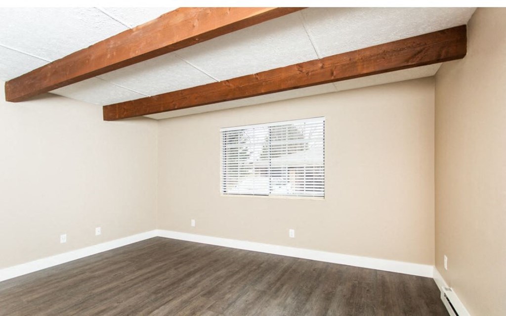 an empty living room with wood flooring and a ceiling beam