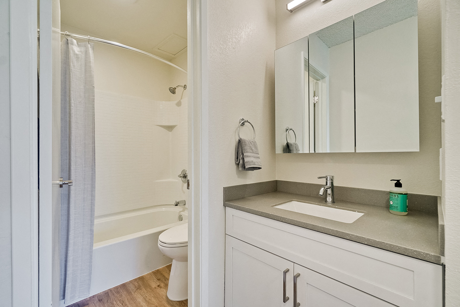 Fremont Apartments-Metro Fremont Apartments Bathroom With Large Three Panel Mirror And White Tile Tub And Wood-Style Flooring