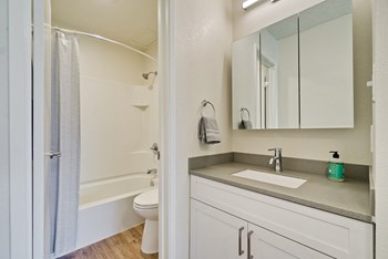 Fremont Apartments-Metro Fremont Apartments Bathroom With Large Three Panel Mirror And White Tile Tub And Wood-Style Flooring - Photo Gallery 8