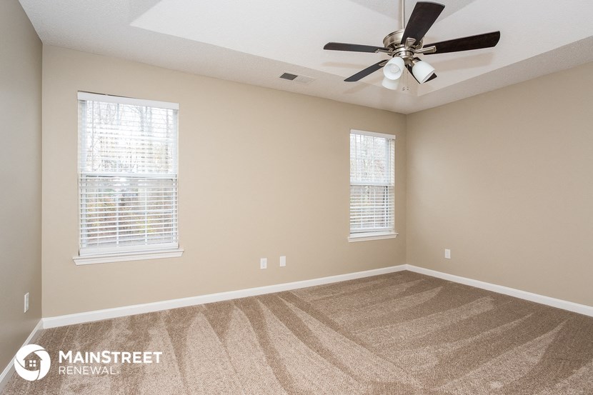 an empty living room with a ceiling fan and two windows