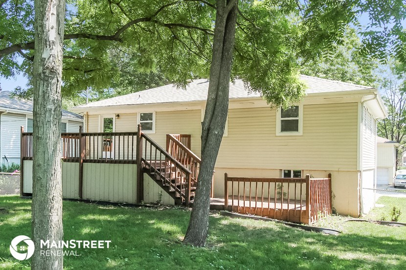 a small yellow house with a deck and trees