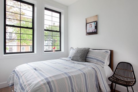 A bedroom with a bed, pillows, a chair, and a picture on the wall.