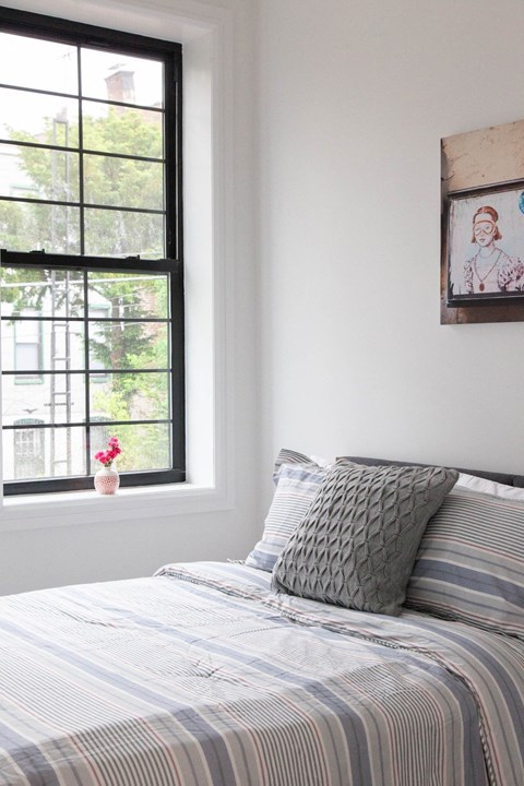 A bed with a striped comforter and a pillow with a diamond pattern sits in front of a window.