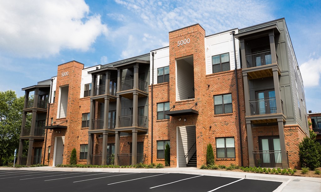 a red brick apartment building with balconies and a parking lot